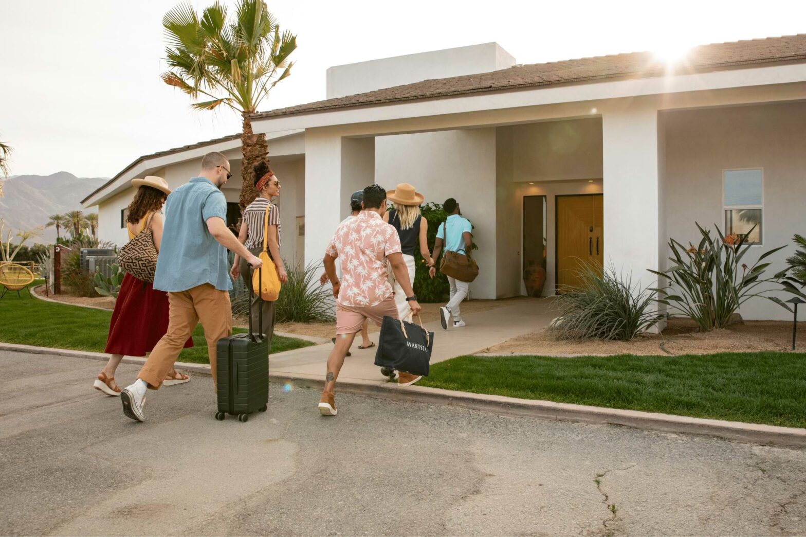 A group of six enter a home; one folding a rolling suitcase, another holding a duffle bag with the word AvantStay