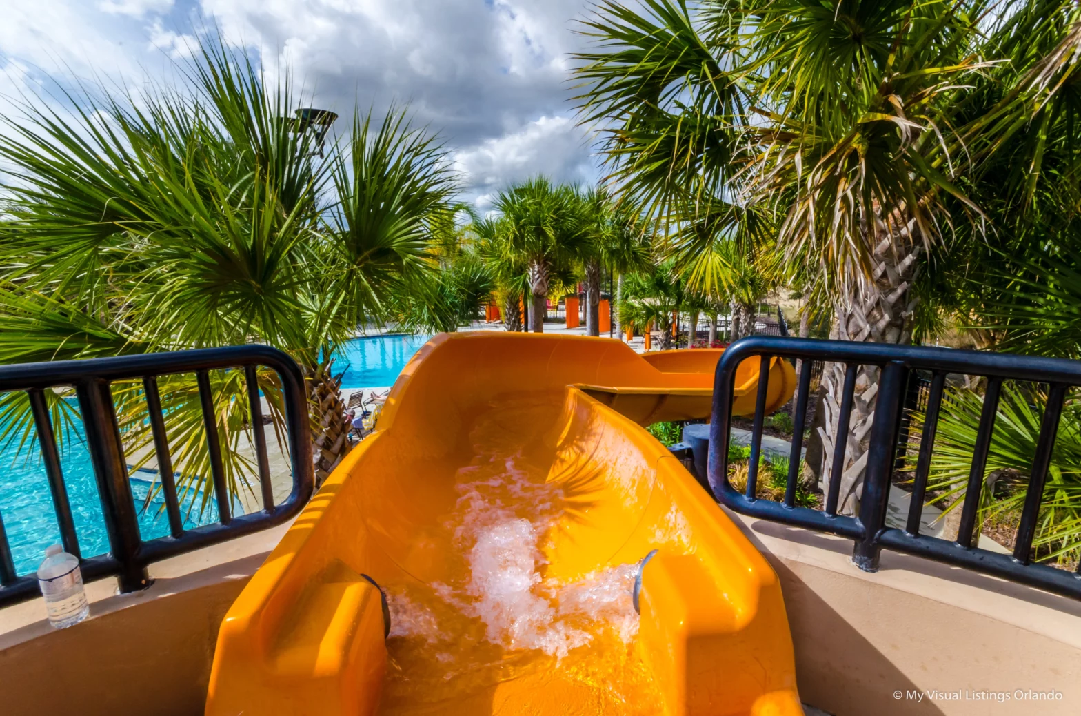orange long slide leading to a big turquoise swimming pool under the summer heat