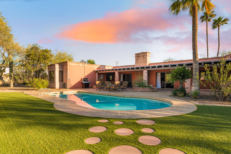 kidney bean shaped swimming pool by the green backyard of a Spanish house making it the best Scottsdale Airbnb