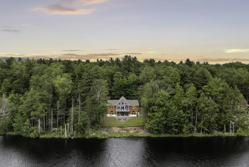 brick mansion house in the middle of the green trees, woods, and in front of a black lake, making it the best poconos airbnb