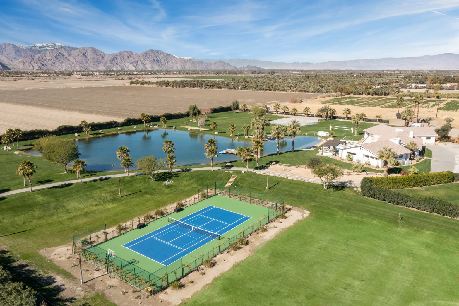 overview shot of a big green yard with blue pickleball court beside a private lake