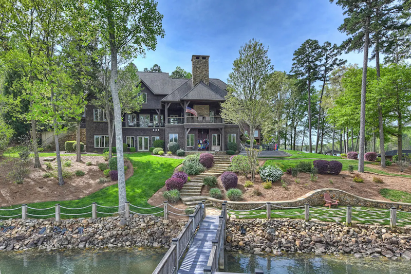 2 story victorian brick mansion with a chimney fronting a green yard and lake that can fit 30 people or more