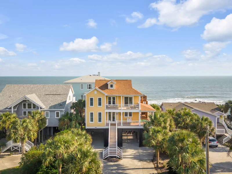 yellow beach house with orange roof and swimming pool in front of the blue ocean of 30a florida