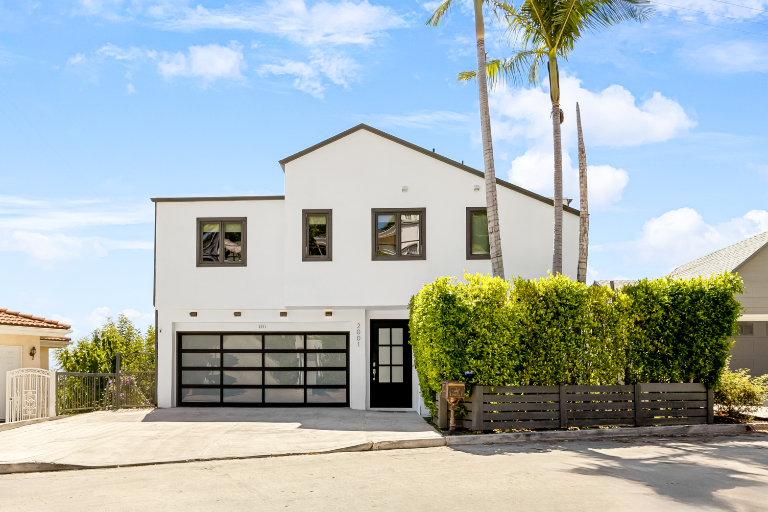 2 story white los angeles airbnb house with a green bush fence