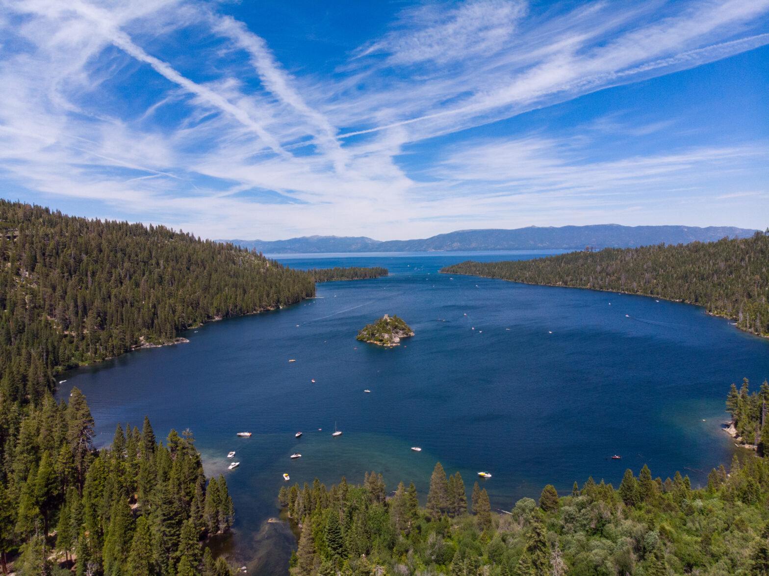 large blue lake surrounded by evergreen pines with streaks of clouds at the sky