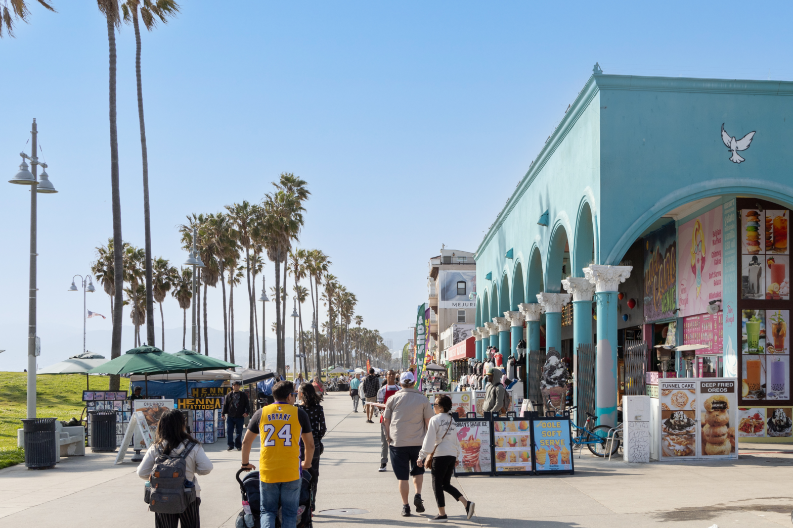 walking alley by the beach and tall palm trees filled by tourists and restaurants