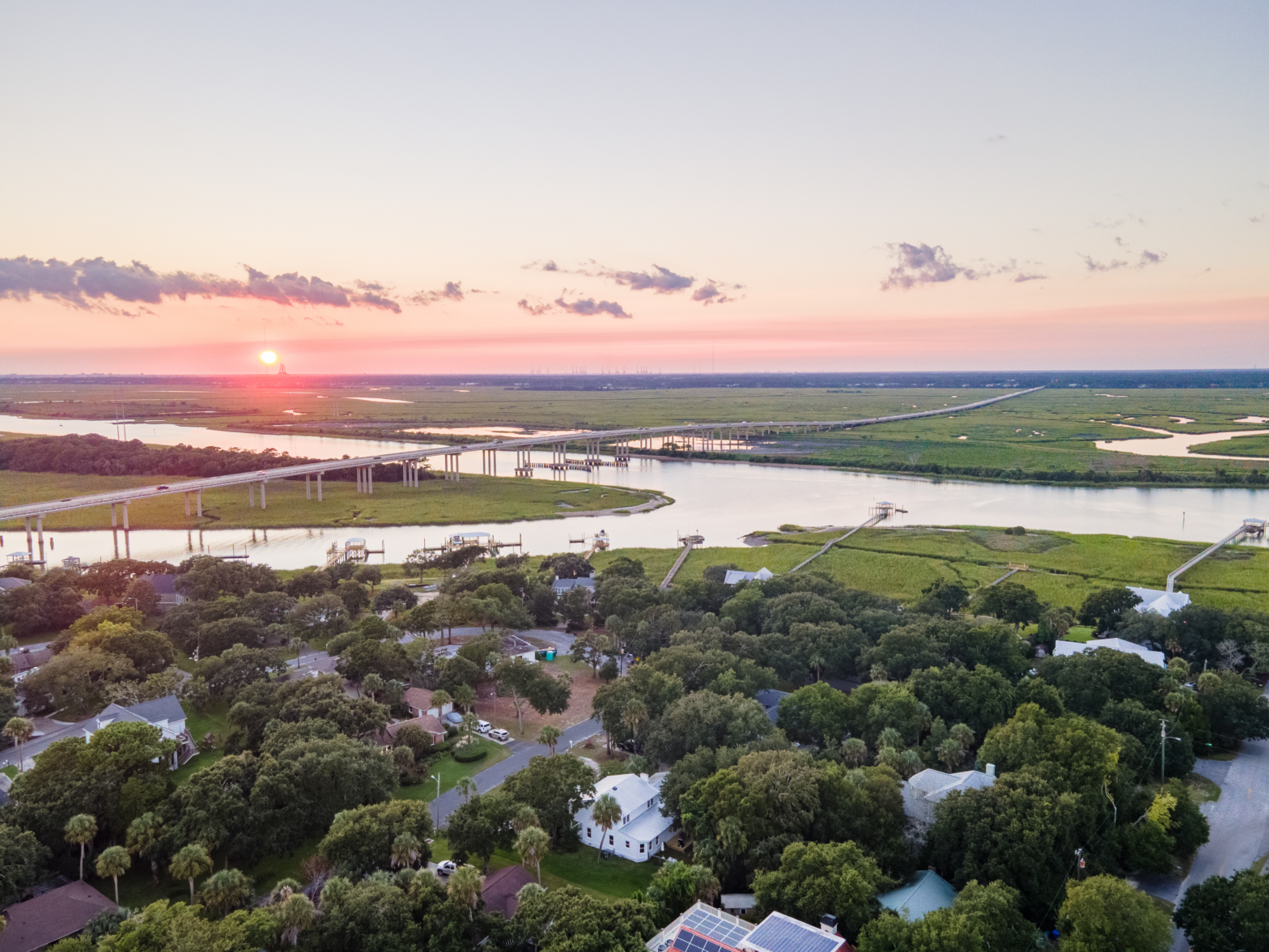 pink skies over the green swamp and river and a train rail crossing the waters