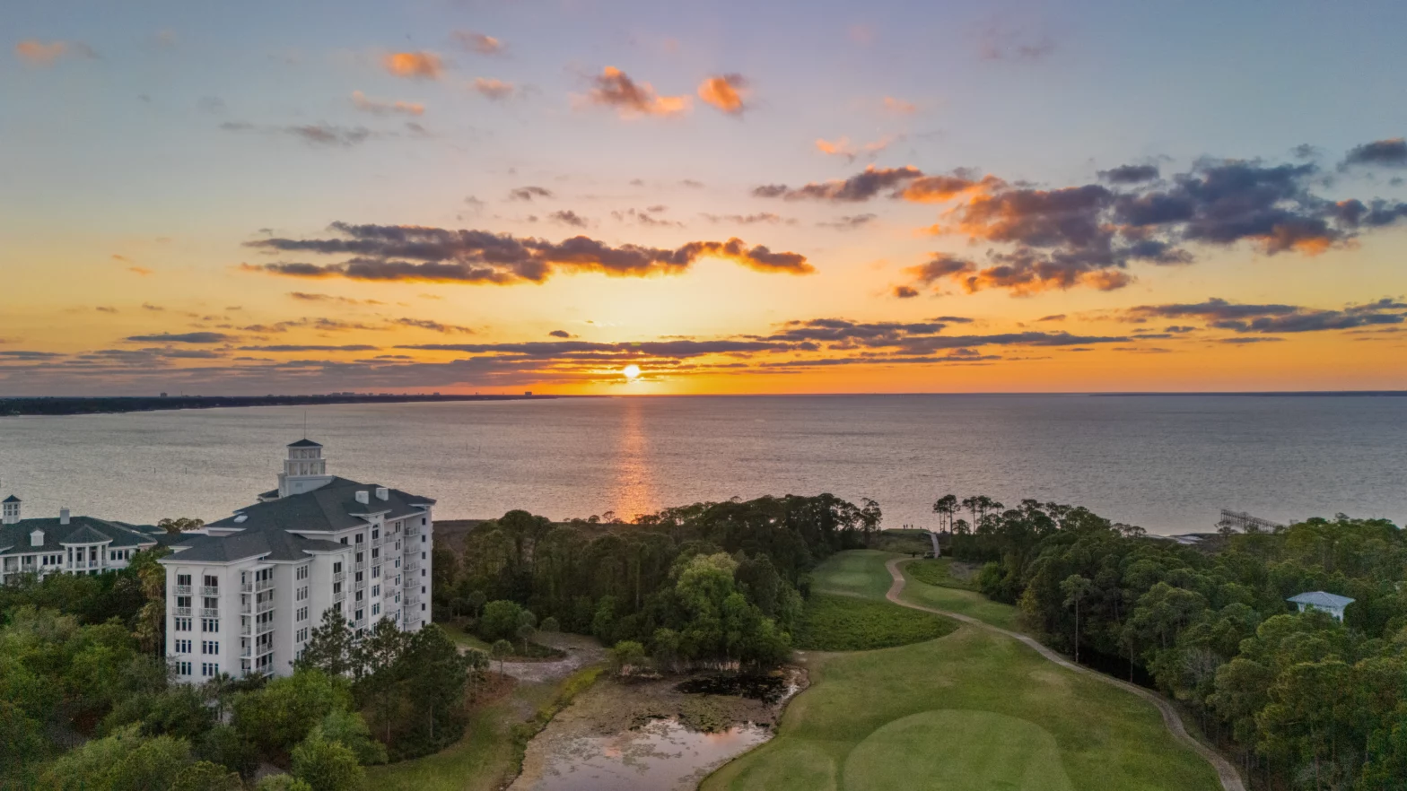 green golf course fronting the beach and orange sunset
