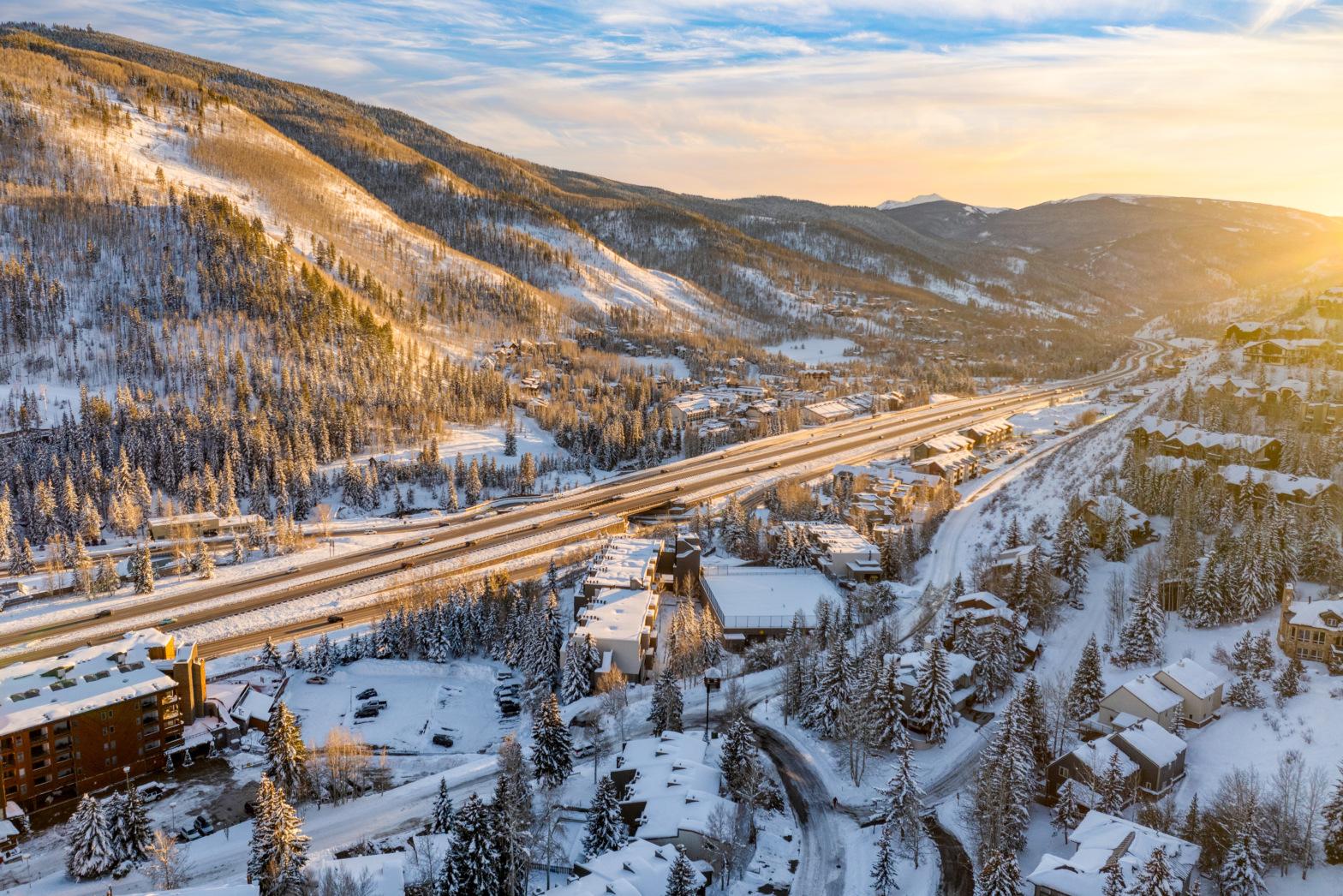 snowy mountain and pine tree forest with a highway road in the middle of the sunrise