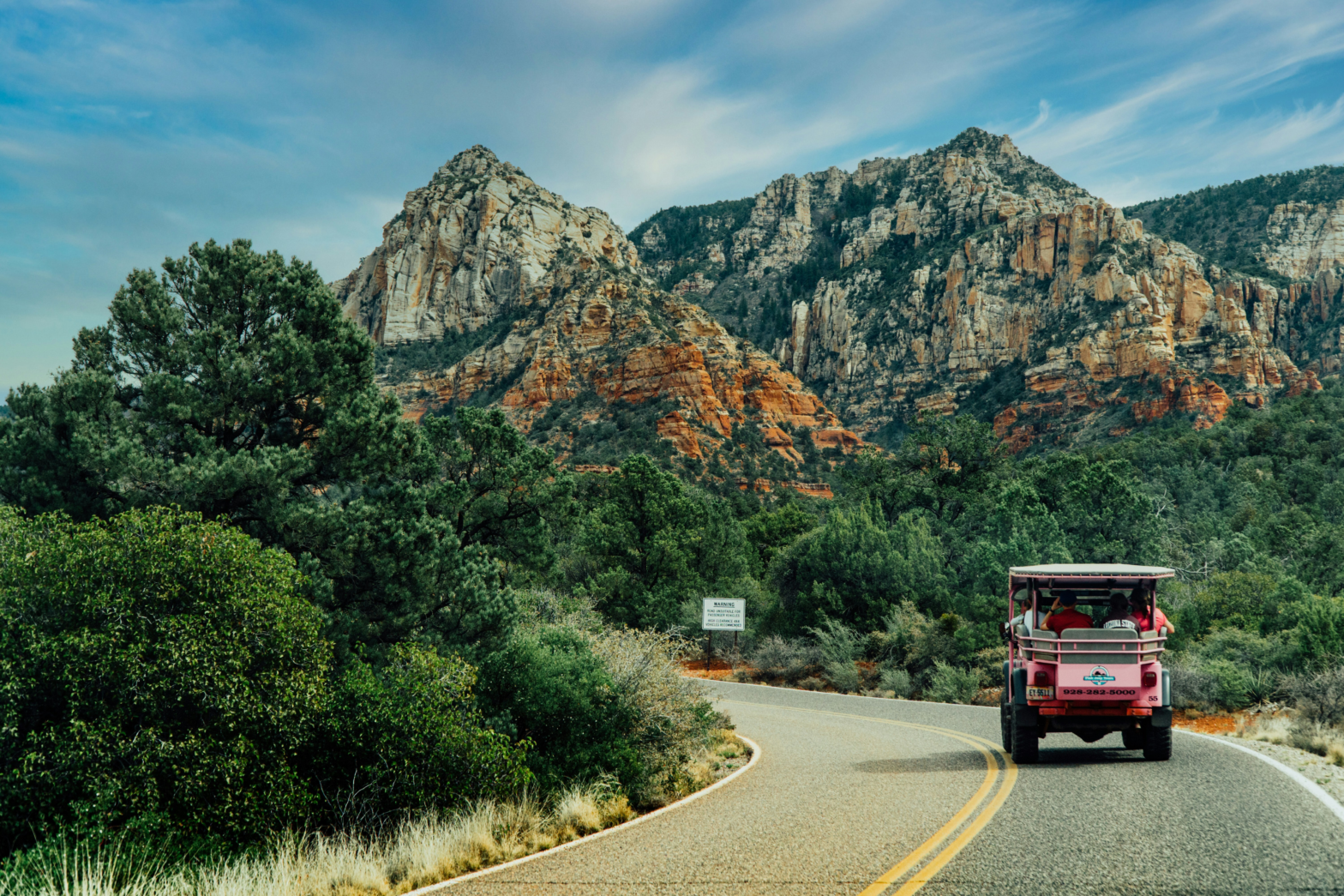 green trees mountain rows and rocks with a golf cart car touring on the road