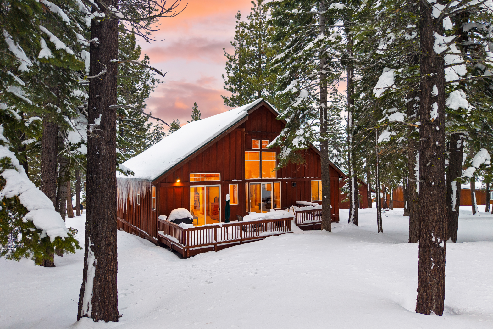 red wood cabin with a snowy rooftop burried in snow and pine trees