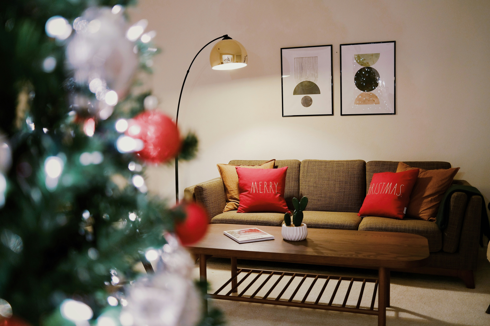 cozy sofa with 2 red pillows saying merry christmas and a blurred christmas tree