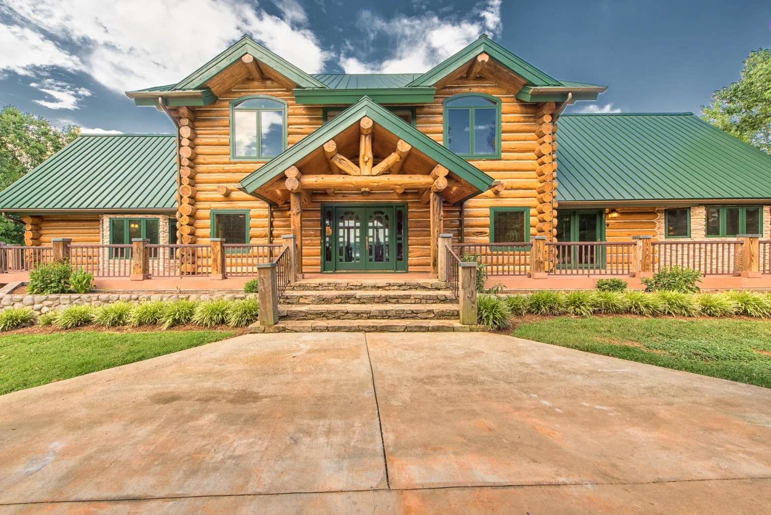 front view of a 2-story log cabin with green roof and lots of windows