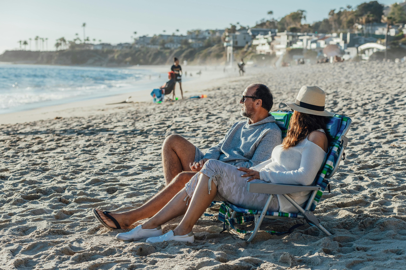 adult and senior couple husband and wife sitting on the beach chair by the white sand shoreline