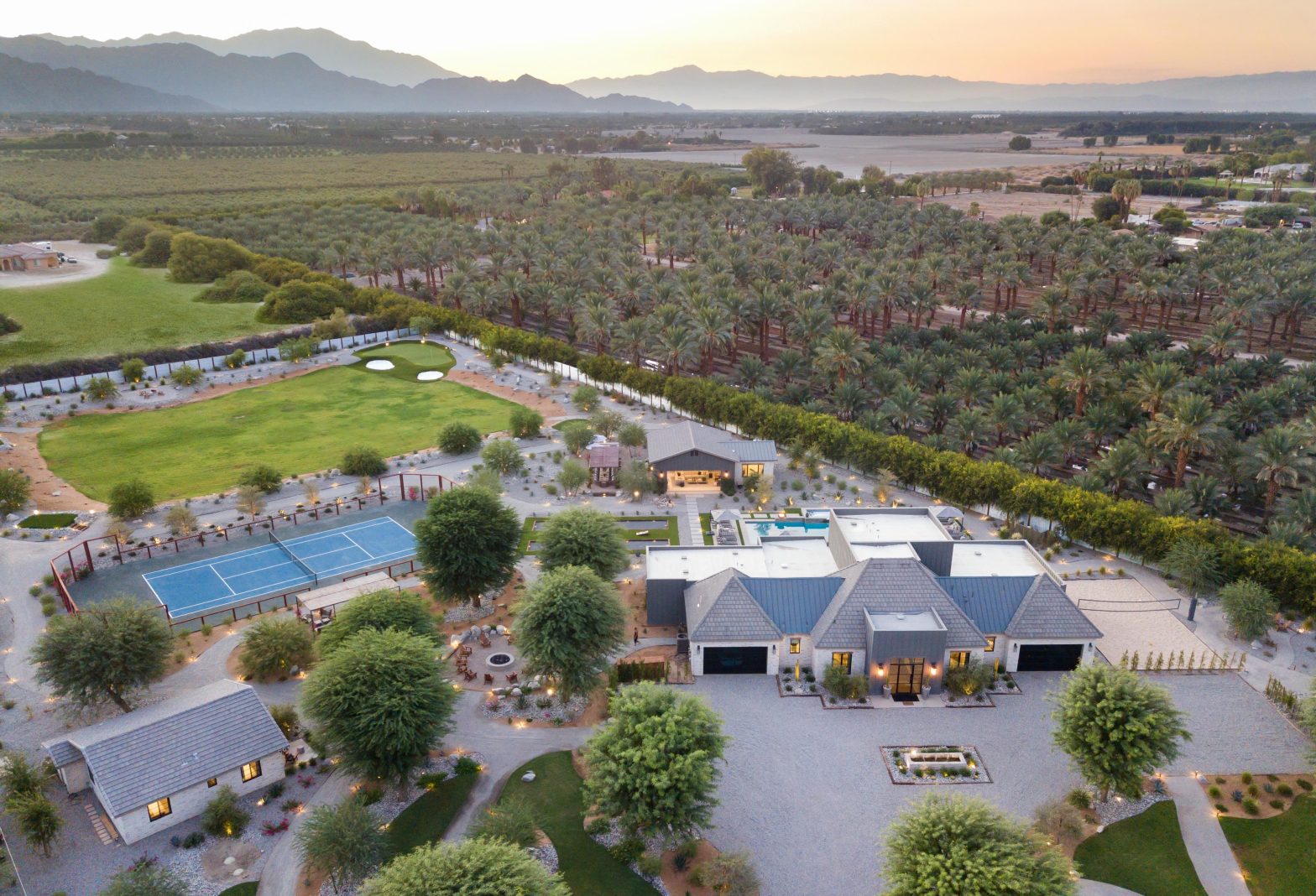 bird's view of a mansion with a big backyard, court, and trees at the background